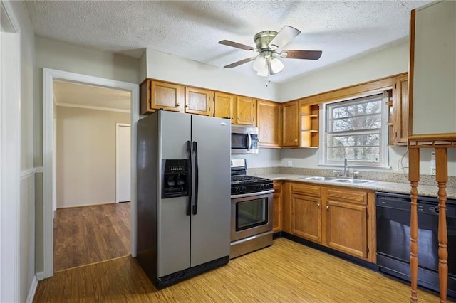 kitchen with light wood finished floors, appliances with stainless steel finishes, brown cabinetry, and a sink