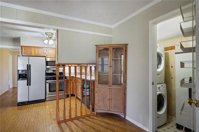 laundry room featuring laundry area, light wood finished floors, stacked washer and clothes dryer, ornamental molding, and a textured ceiling