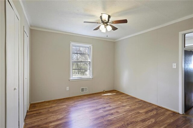 unfurnished bedroom with ceiling fan, ornamental molding, wood finished floors, and visible vents