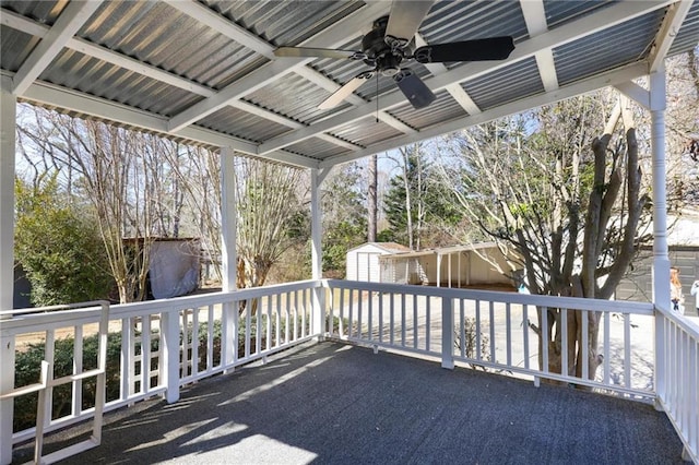 wooden terrace featuring a ceiling fan, an outdoor structure, a patio, and a storage unit