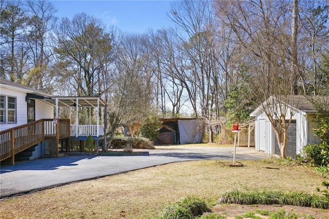 view of yard featuring an outbuilding, driveway, a storage shed, and a deck