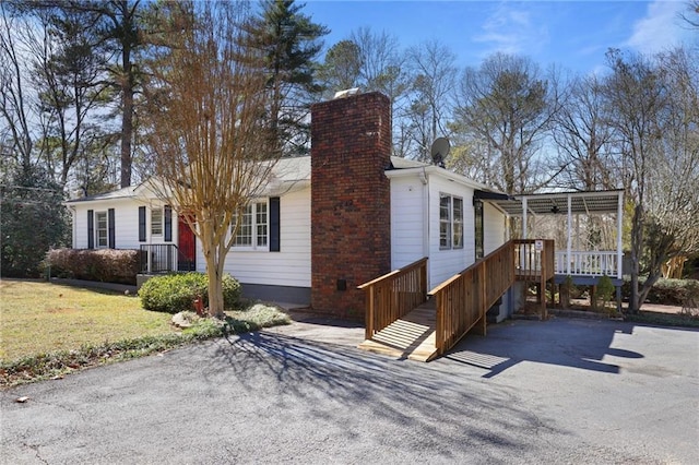 view of side of property with an attached carport, a chimney, aphalt driveway, and a lawn