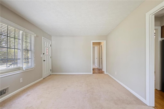 empty room with a textured ceiling, carpet, visible vents, and baseboards