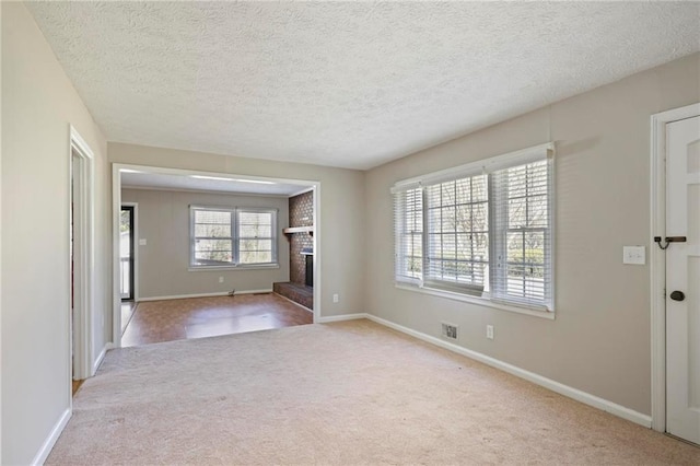 unfurnished room with visible vents, baseboards, carpet, a textured ceiling, and a brick fireplace