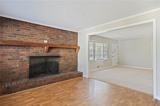 unfurnished living room with a textured ceiling, wood finished floors, baseboards, a brick fireplace, and crown molding