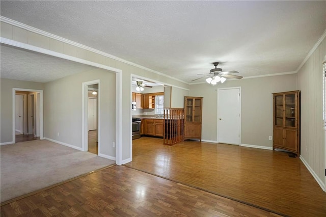 unfurnished living room with crown molding, a textured ceiling, baseboards, and wood finished floors