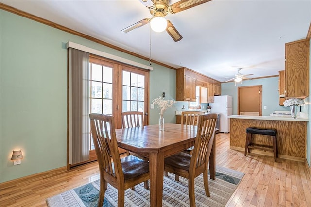 dining room with a ceiling fan, light wood-type flooring, crown molding, and baseboards