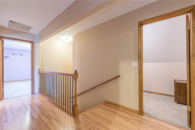 hallway with baseboards, visible vents, wood finished floors, and an upstairs landing