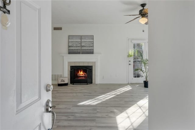 living room with a tiled fireplace, light hardwood / wood-style flooring, and ceiling fan