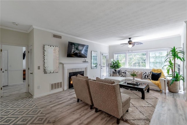 living room featuring a tiled fireplace, light hardwood / wood-style flooring, ornamental molding, and ceiling fan