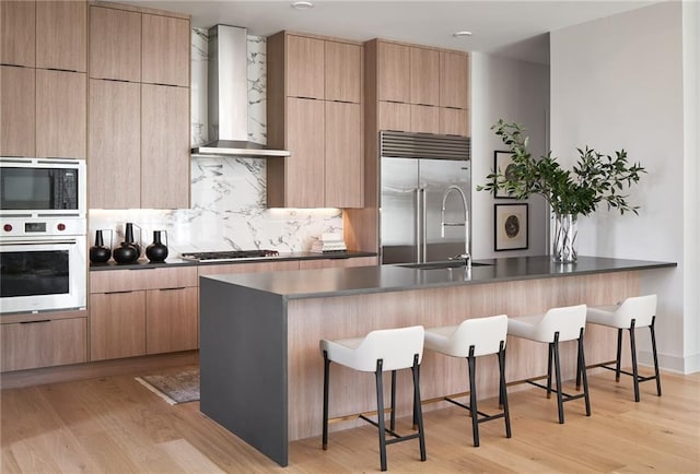 kitchen with a kitchen breakfast bar, light hardwood / wood-style flooring, wall chimney exhaust hood, and built in appliances