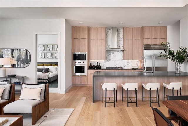 kitchen featuring tasteful backsplash, wall chimney range hood, black appliances, light hardwood / wood-style flooring, and sink