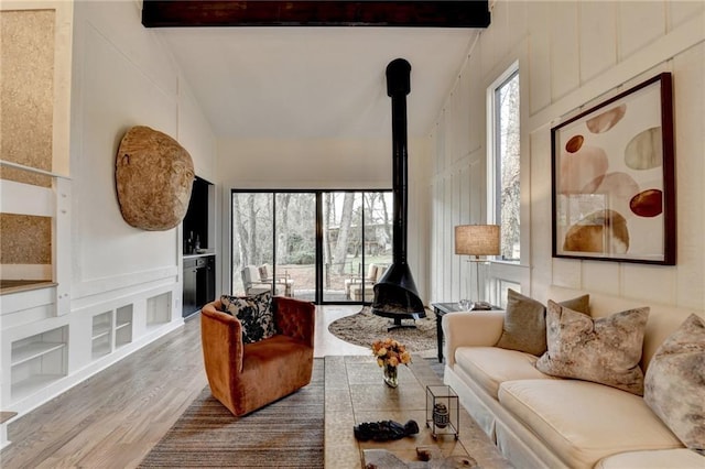 living room featuring beamed ceiling, plenty of natural light, hardwood / wood-style flooring, and a wood stove