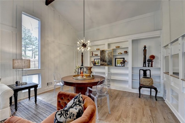 dining area featuring built in shelves, vaulted ceiling, an inviting chandelier, and light wood-type flooring