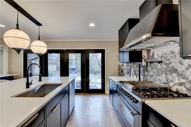 kitchen with wall chimney range hood, sink, appliances with stainless steel finishes, hanging light fixtures, and light stone countertops