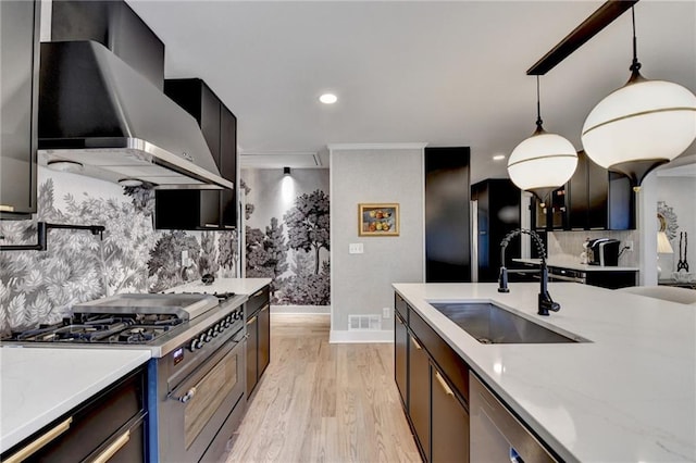 kitchen featuring sink, hanging light fixtures, stainless steel appliances, light stone countertops, and wall chimney exhaust hood