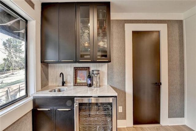 bar with dark brown cabinets, sink, beverage cooler, and light hardwood / wood-style flooring