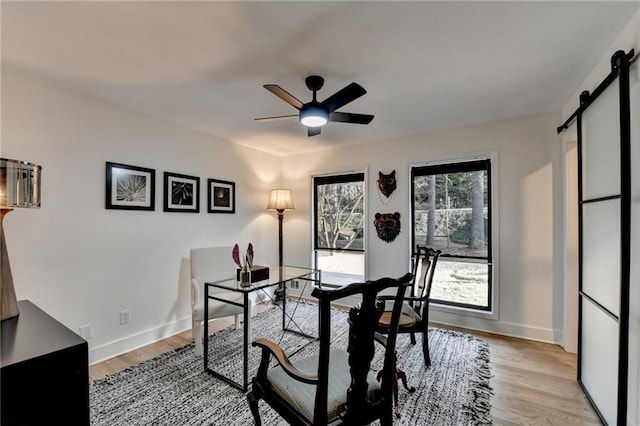 dining area with a barn door, light wood-type flooring, and ceiling fan