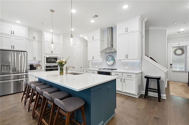 kitchen with wall chimney exhaust hood, stainless steel appliances, a kitchen island with sink, sink, and decorative light fixtures