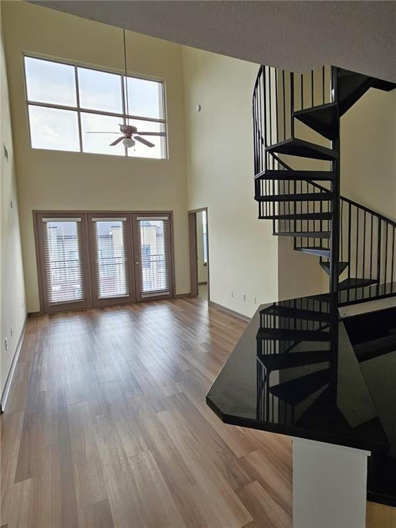 living area featuring a ceiling fan, stairway, a high ceiling, wood finished floors, and baseboards