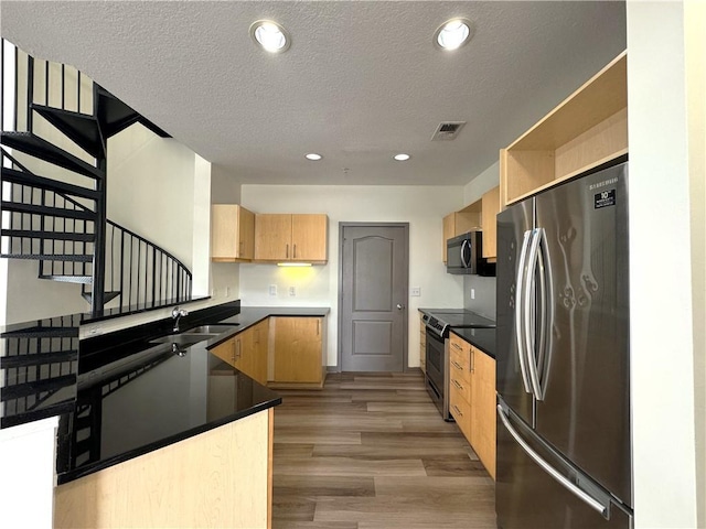 kitchen with stainless steel appliances, a sink, light brown cabinetry, light wood-style flooring, and a textured ceiling