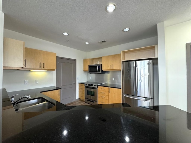 kitchen featuring appliances with stainless steel finishes, a sink, light brown cabinets, recessed lighting, and a textured ceiling