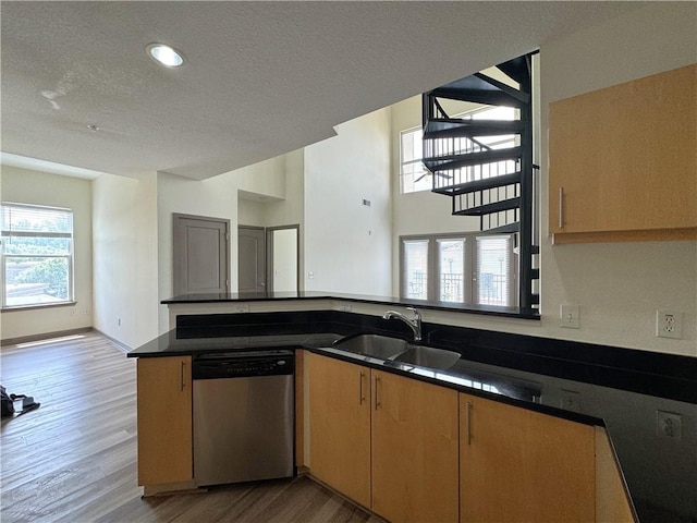 kitchen featuring stainless steel dishwasher, a sink, wood finished floors, a textured ceiling, and a peninsula