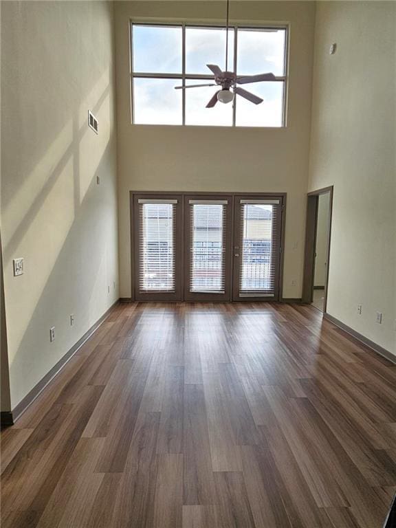 unfurnished living room with a towering ceiling, ceiling fan, french doors, wood finished floors, and baseboards