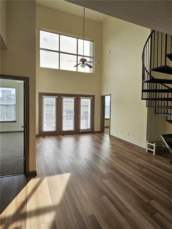 unfurnished living room featuring wood finished floors, a ceiling fan, stairway, and a towering ceiling