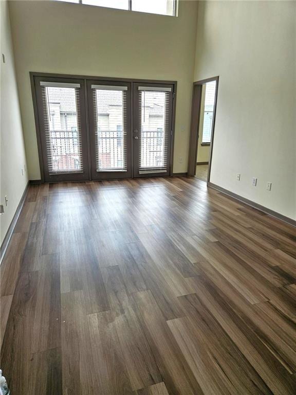 unfurnished living room featuring dark wood-type flooring, a high ceiling, french doors, and baseboards