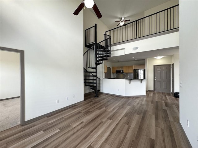 unfurnished living room with wood finished floors, a towering ceiling, a ceiling fan, stairway, and baseboards