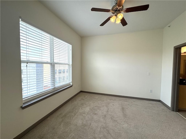 empty room featuring light colored carpet, baseboards, and a ceiling fan