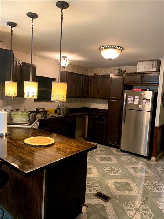 kitchen with kitchen peninsula, stainless steel fridge, decorative light fixtures, and dark brown cabinets