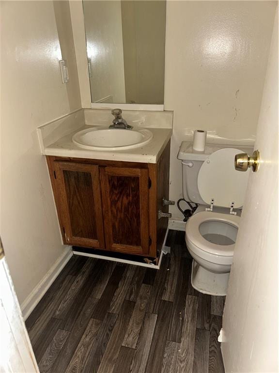 half bath with toilet, baseboards, wood finished floors, and vanity