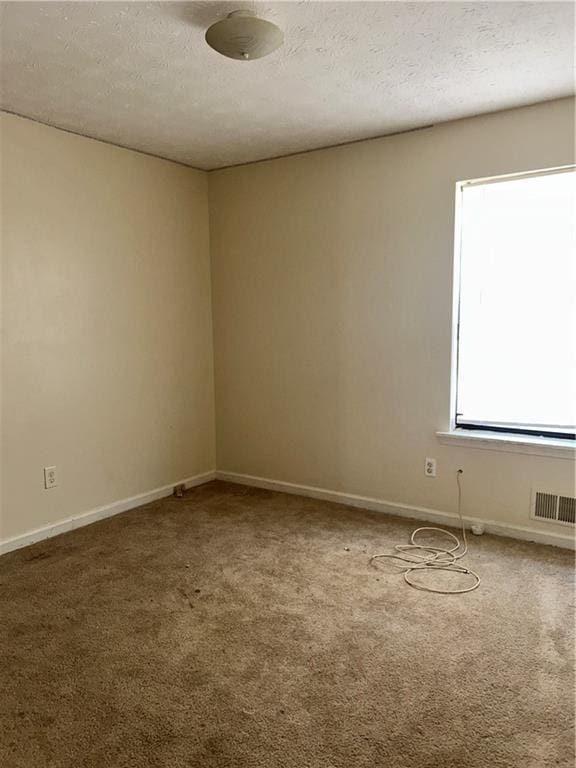 empty room with carpet floors, baseboards, and a textured ceiling