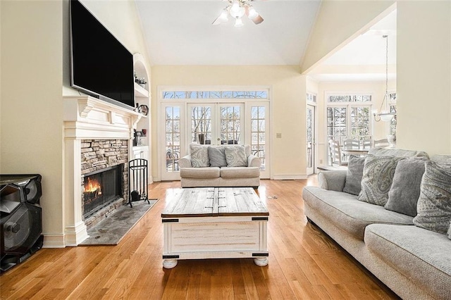 living area featuring a ceiling fan, high vaulted ceiling, a stone fireplace, hardwood / wood-style flooring, and french doors