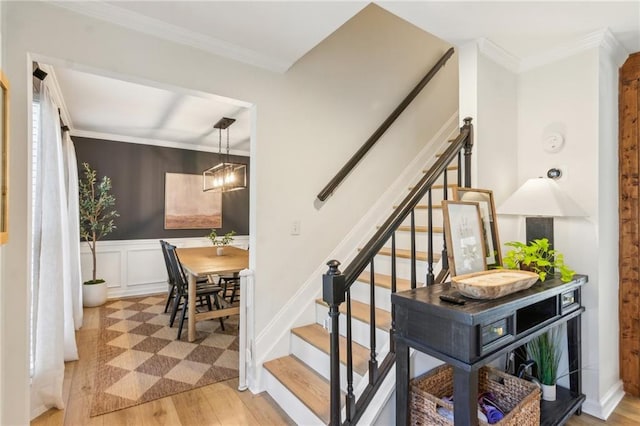 stairway with a decorative wall, wood finished floors, a wainscoted wall, and ornamental molding