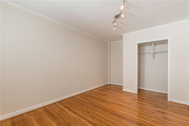 unfurnished bedroom with wood-type flooring, crown molding, and a closet