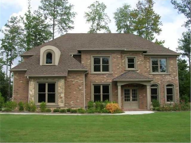 view of front of house with a front yard, french doors, a shingled roof, and brick siding