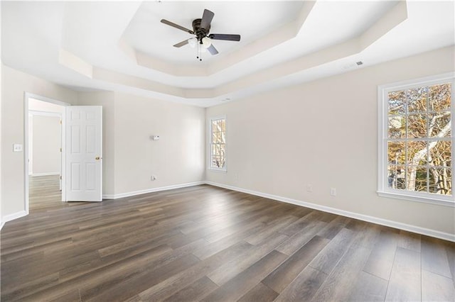empty room with a tray ceiling, baseboards, dark wood finished floors, and a wealth of natural light