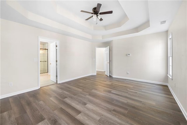 empty room with visible vents, ceiling fan, a raised ceiling, and wood finished floors