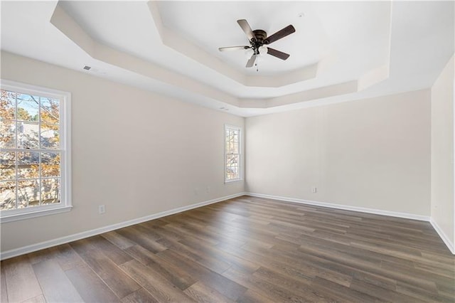 spare room with baseboards, a ceiling fan, dark wood-type flooring, visible vents, and a raised ceiling
