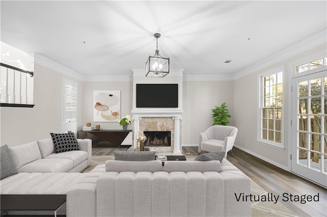 living area with crown molding, an inviting chandelier, a fireplace, wood finished floors, and baseboards