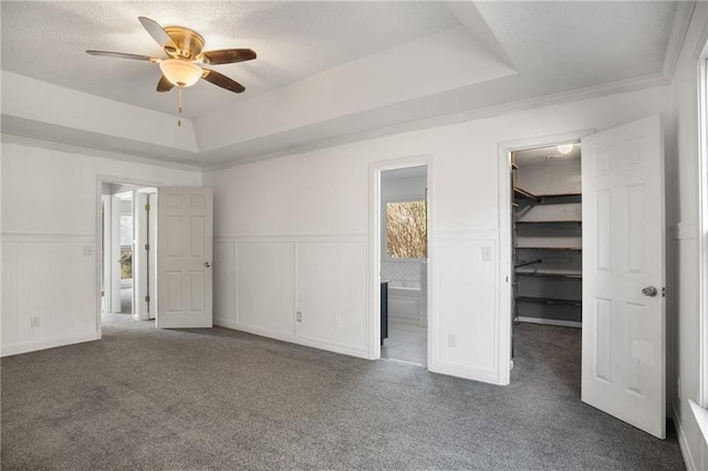 unfurnished bedroom with dark carpet, connected bathroom, a tray ceiling, and a spacious closet