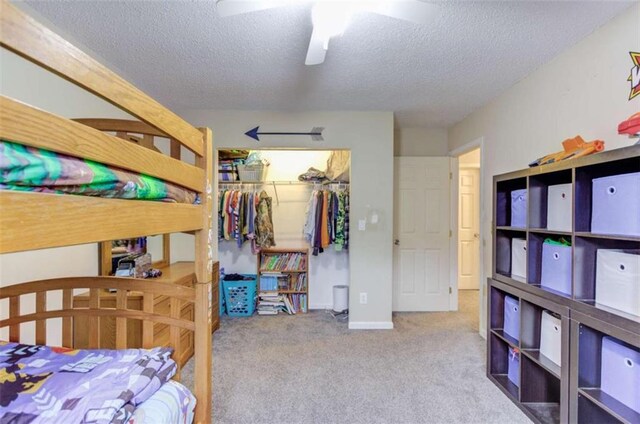 carpeted bedroom with ceiling fan, a closet, a spacious closet, and a textured ceiling