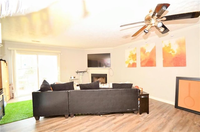 living area with light wood-type flooring, ornamental molding, a fireplace, baseboards, and ceiling fan