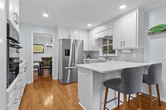 kitchen featuring stainless steel refrigerator with ice dispenser, a sink, a peninsula, white cabinetry, and decorative backsplash