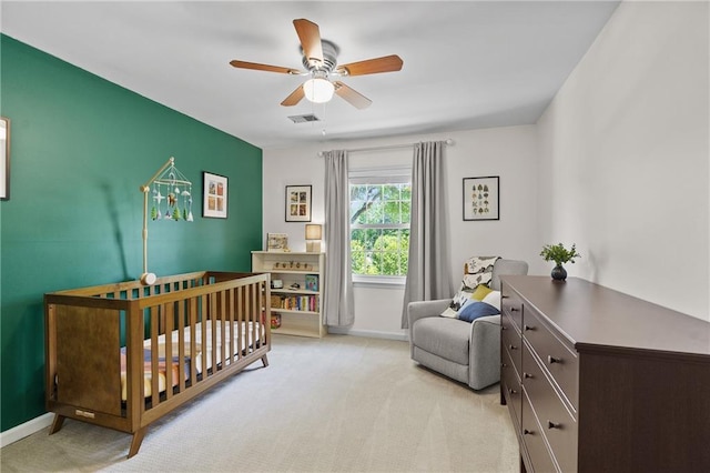 bedroom featuring a nursery area, light carpet, baseboards, and a ceiling fan