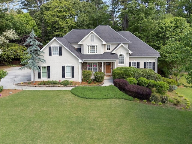 view of front of property featuring roof with shingles, stucco siding, driveway, and a front yard
