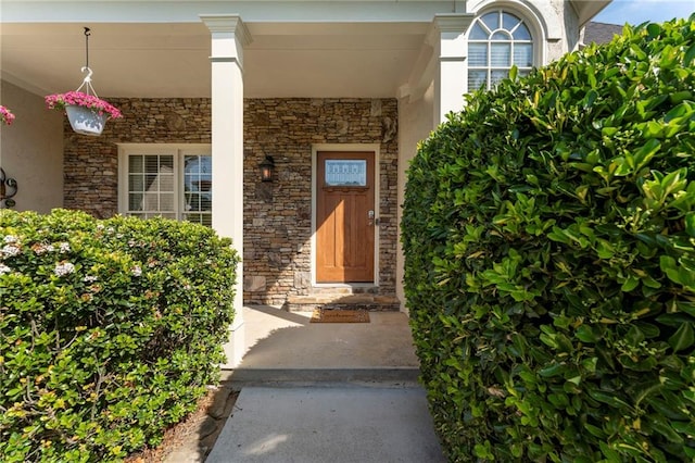 view of exterior entry with covered porch, stone siding, and stucco siding